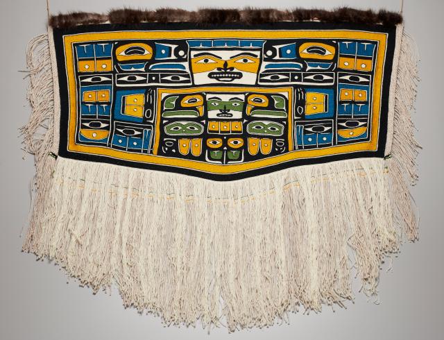A large woven artwork with Indigenous motifs. It hangs flat on a wall.