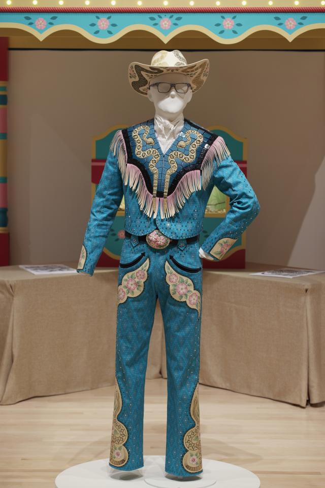 Mannequin wearing a denim fabric and embellished suit and a ceramic hat.