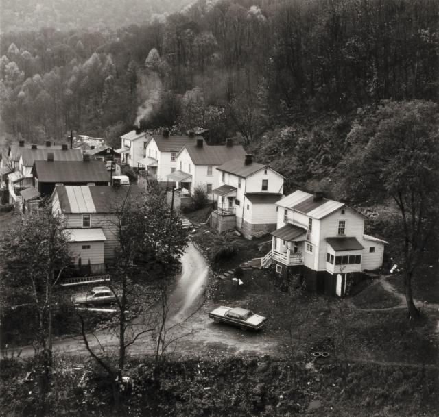 Black and white photograph of a row of houses nestled in the foothills of mountains.