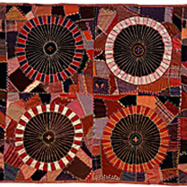 This is an embroidered wool quilt with red color tones and four circles. 