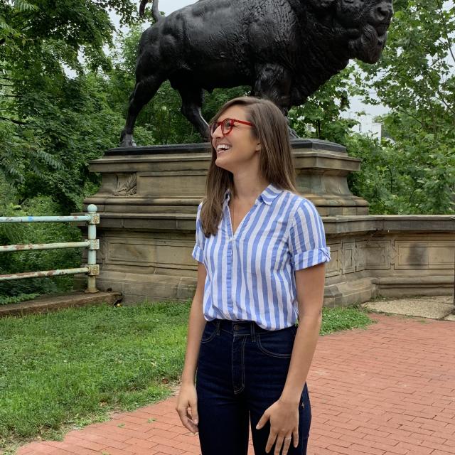 A photograph of a woman standing in front of a sculpture of a bison