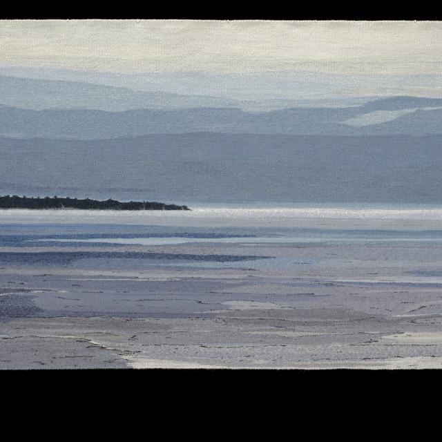 A textile work depicting a landscape with water, land, and mountains.