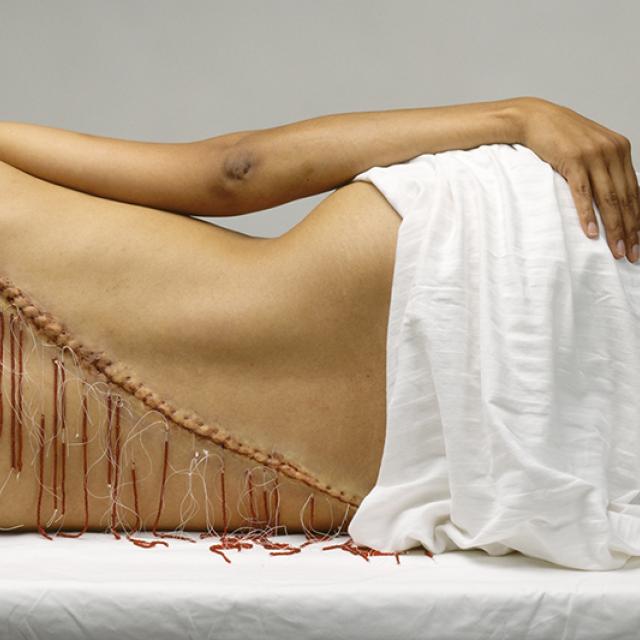 A figure laying on it's side with a diagonal line down it's back with red thread.