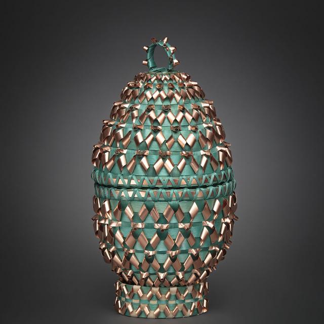A oval artwork with green and gold material woven into it. 