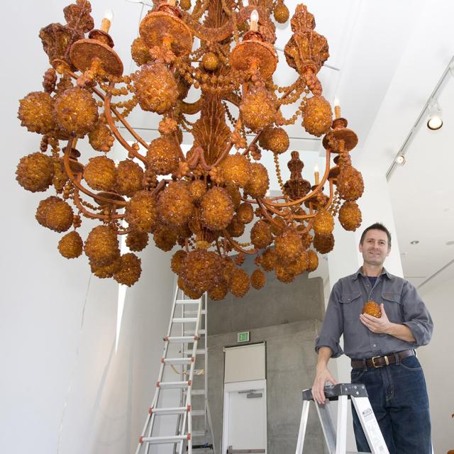 A photograph of an artist in a gallery with their work. 