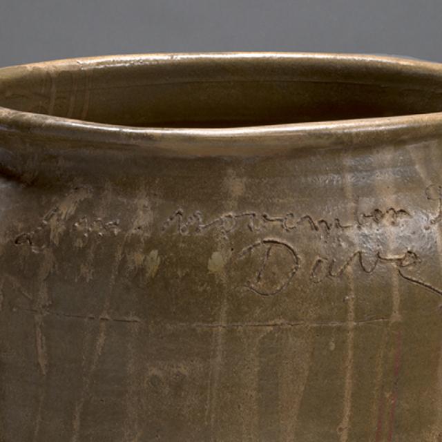 Detail of brown ceramic jar with writing and the signature "Dave" inscribed around the top.