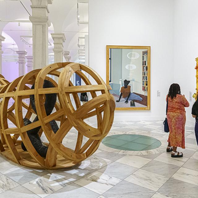 Two visitors looking at an abstract painting. There are artworks around them.