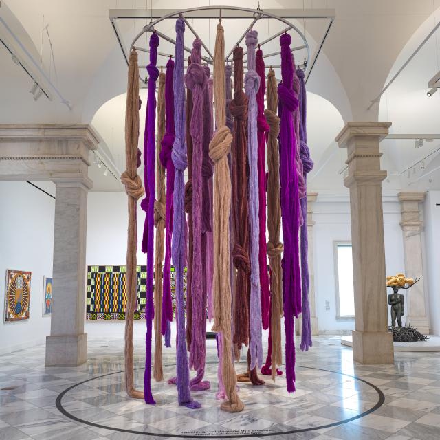 A hanging installation of vibrant locks of fiber in pinks and purples.