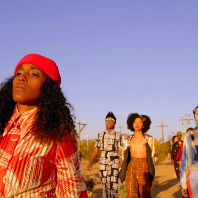 A person walks holding a radio near her face. A group of people follow.