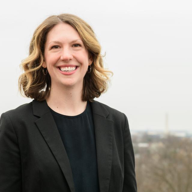 A woman in a black blazer smiles in front of a dusky landscape