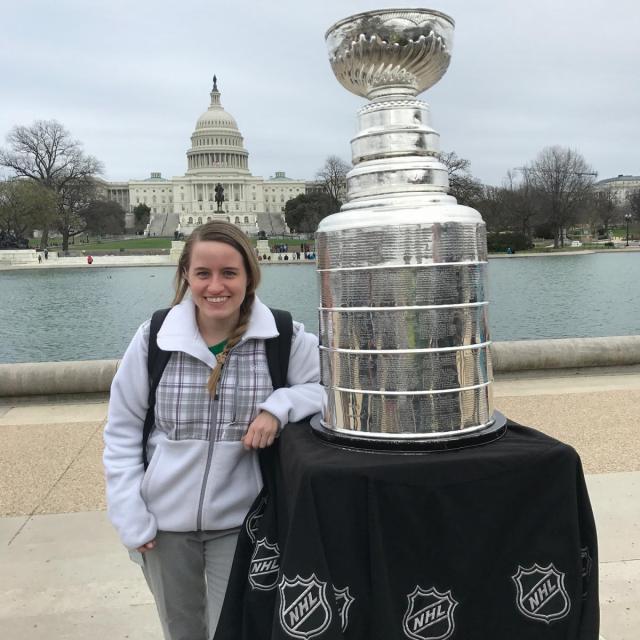 This is an image of a woman next to the Stanley Cup with the capital in the background.